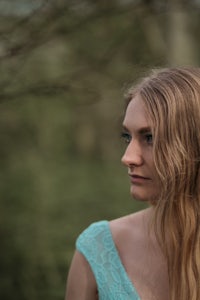 a woman in a blue dress is standing in the woods
